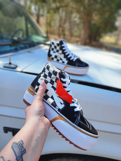 Checkered high-top sneakers held in front of a white car with trees in the background