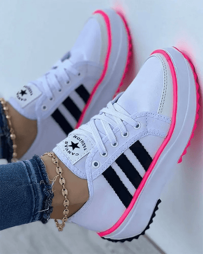 White sneakers with black stripes and pink soles worn by a person.